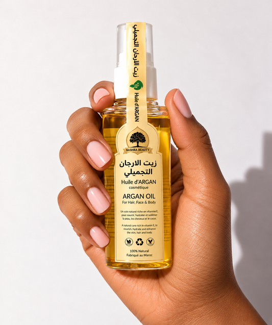 Hand holding Bashra Beauty golden argan oil with its Moroccan-inspired label against a clean, softly lit background.