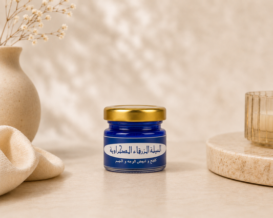 Bashra Beauty Sahara Blue Nila Powder in a blue glass jar with a gold lid displayed on a warm beige spa-inspired background for natural skin brightening and skincare.