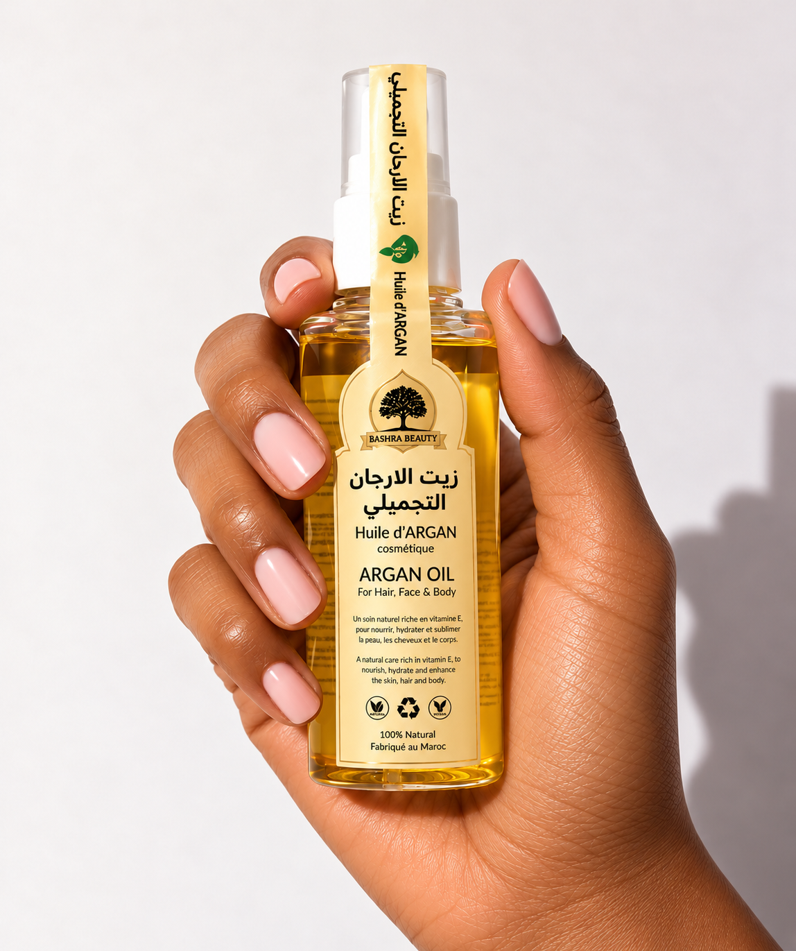 Hand holding Bashra Beauty golden argan oil with its Moroccan-inspired label against a clean, softly lit background.