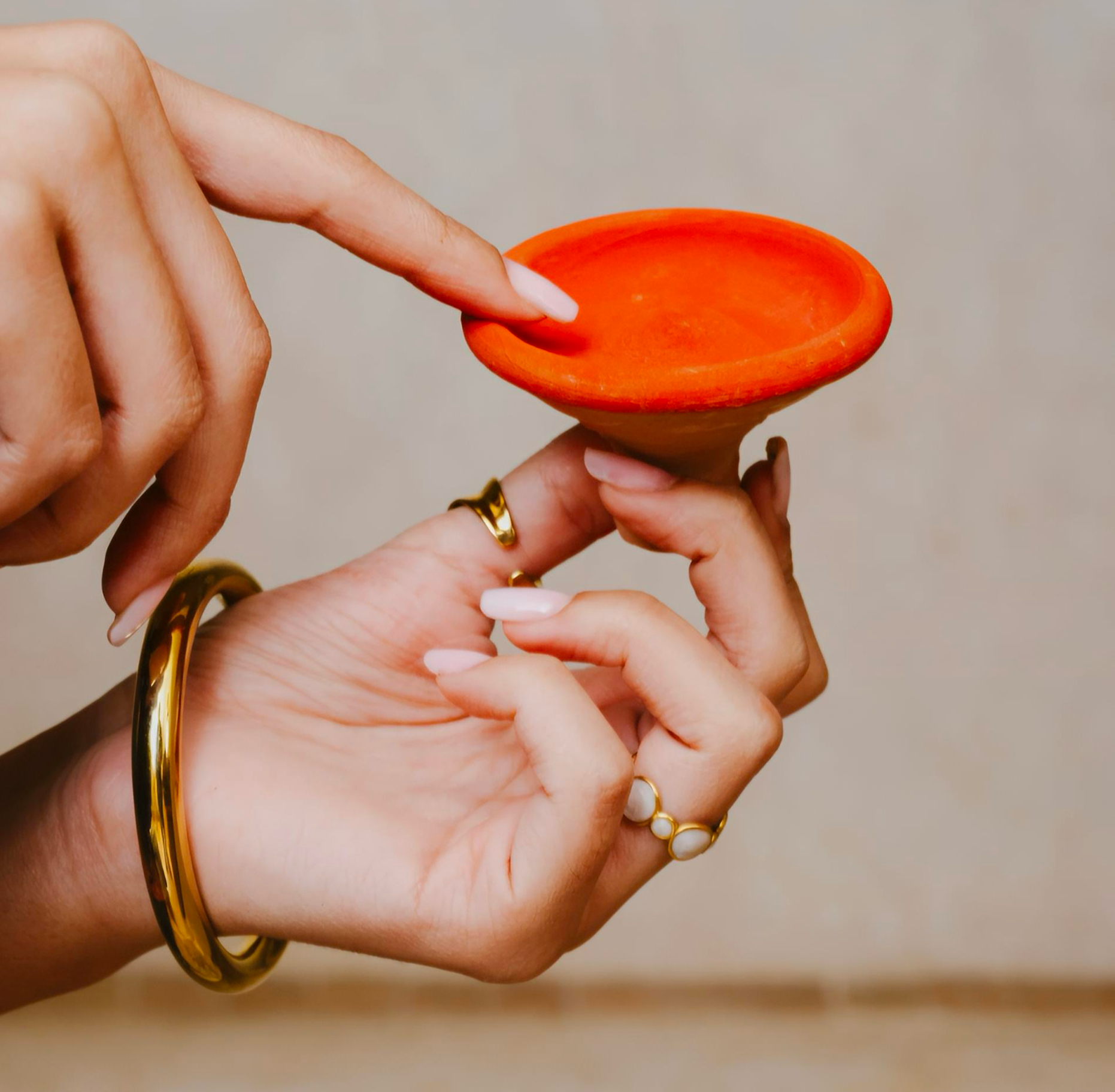 Hands with gold rings and bracelet dipping a finger into a small orange-red Sudanese clay lip color pot