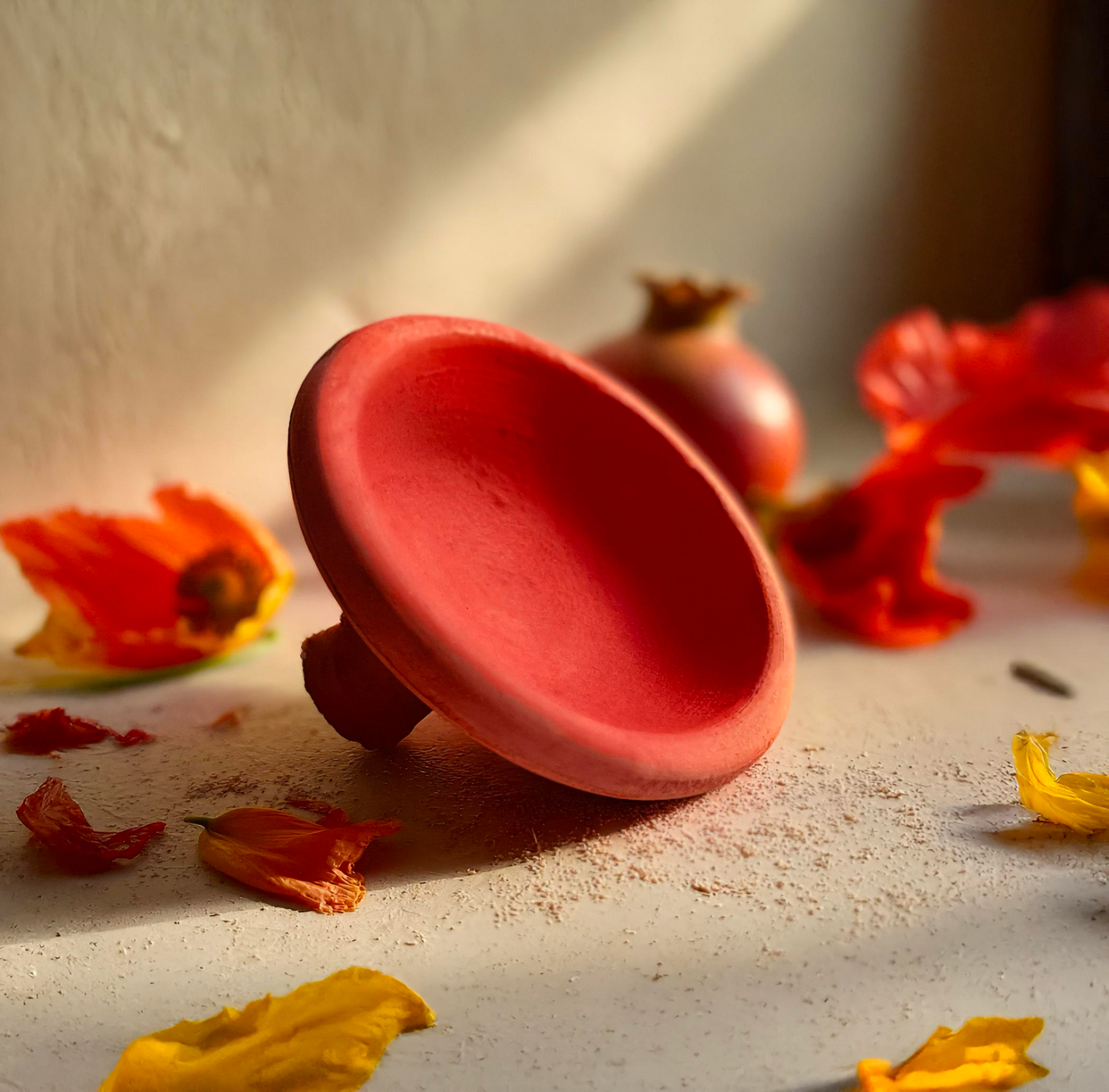 Moroccan clay lip color pot surrounded by pomegranate and flower petals in warm natural light