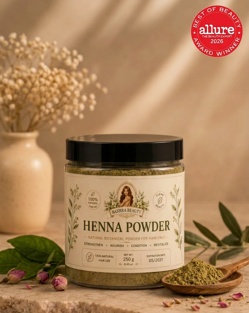 Bashra Beauty Henna Powder in a clear jar with a black lid and botanical label, displayed on a warm beige stone surface with natural henna powder and dried botanicals.