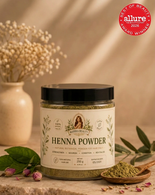 Bashra Beauty Henna Powder in a clear jar with a black lid and botanical label, displayed on a warm beige stone surface with natural henna powder and dried botanicals.
