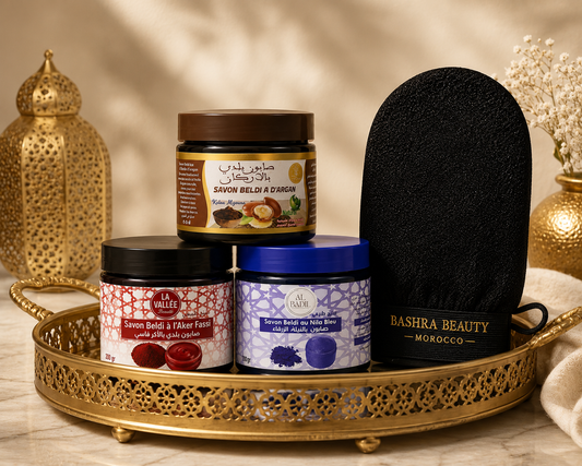 Bashra Beauty Moroccan Beldi Soap collection featuring Argan, Aker Fassi, and Blue Nila Beldi Soaps with a traditional Kessa exfoliating glove displayed on an elegant gold tray for an authentic Moroccan hammam skincare ritual.
