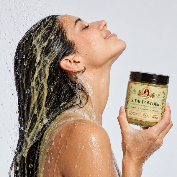 Bashra Beauty Sidr Powder jar held by a woman rinsing light green sidr treatment from her long black hair in the shower.